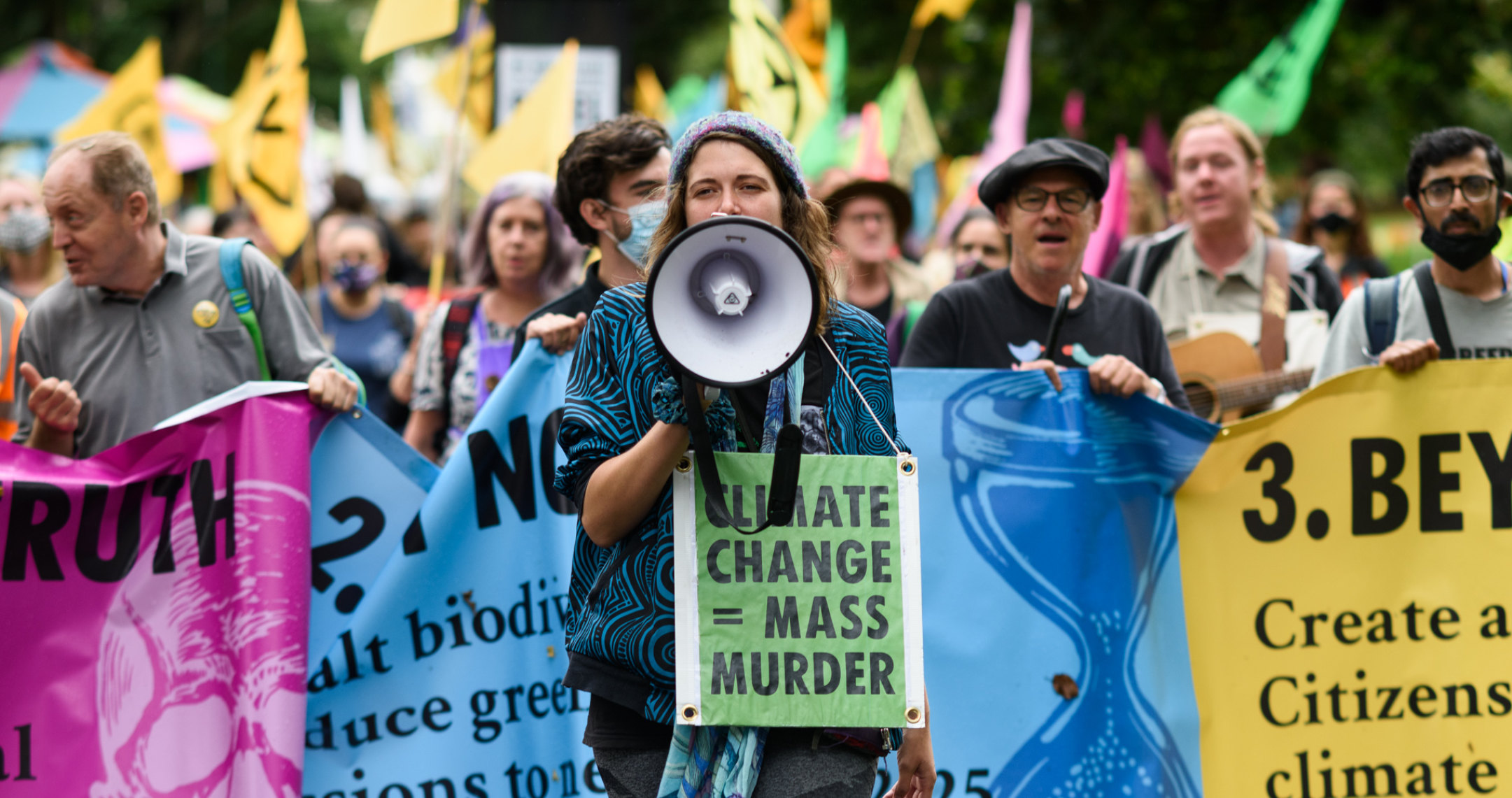 A woman speaking into a megaphone in front of a group of protesters holding a banner