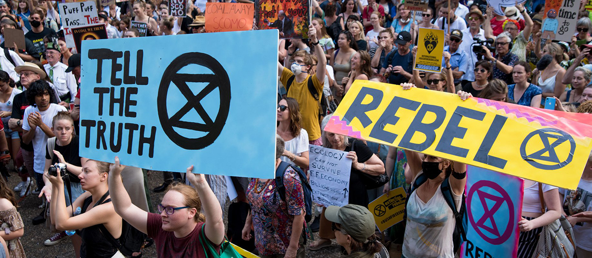 Extinction Rebellion members at a rally holding signs reading "Tell the truth" and "Rebel"